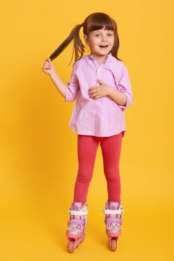 Gülümseyen mutlu kadın, sarı arka planda yalnız poz veriyor, tozluk ve günlük gömlek giyiyor, çocuk at kuyruğuna dokunuyor, uydu kamerasına bakıyor, çocuk pateni yapıyor..