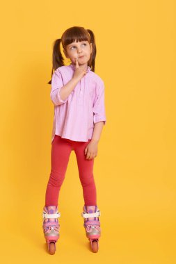 Hoş, sevimli bir çocuk patenlerle kameraya bakıyor, aktif bir şekilde vakit geçiriyor, düşünceli bir yüz ifadesi takınıyor, parmağını yanağında tutuyor..