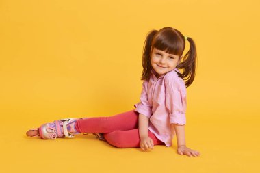 Yerde paten kayan beyaz, atkuyruklu, sarı arka planda izole edilmiş, gömlek ve taytlı, sevimli, beyaz bir kadın..