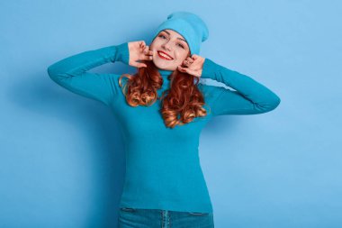 Kıvırcık saçlı mutlu tatlı kız ellerini kaldırıyor ve doğrudan kameraya bakıyor. Mavi elbiseli kızıl kadın, olumlu duyguları olan büyüleyici kadın..
