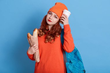 Dersten sonra atıştıracak bir şeyler bulan yorgun öğrenci, kameraya üzgün bir ifadeyle bakıyor, çalıştıktan sonra yorgun düşüyor, kadın turuncu kazak ve şapka giyiyor, kafasının yanına gitmek için kahve tutuyor ve uzun bir somun ekmek yiyor..