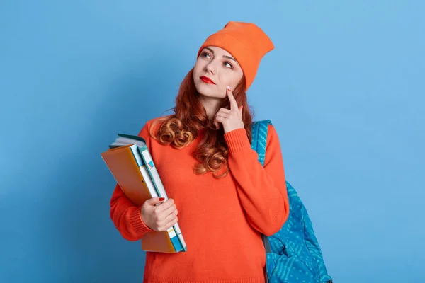 沉思的白人女孩的画像 表情深沉 专注于重要的任务 手指放在脸颊上 身穿橙色连衣裙 头戴帽子 进入大学 — 图库照片