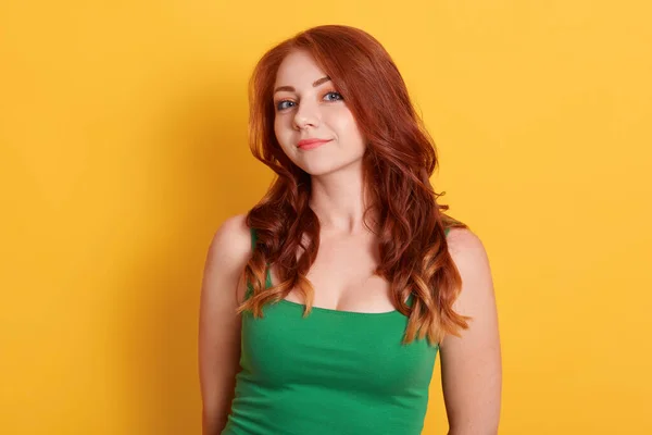 穿着休闲绿色无袖T恤 留着卷发的红头发女模的画像 直勾勾地望着相机 在黄色的墙壁上摆姿势 — 图库照片