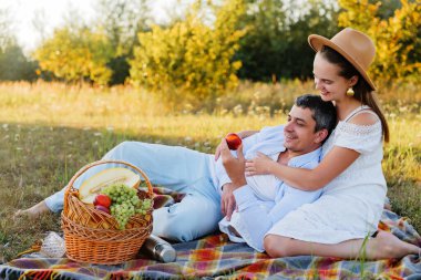 İki insan piknik sırasında neşe dolu bir anı paylaşıyor. Canlı yeşil bir alanda. Güneş ışığı ve doğanın güzelliğiyle dolu..