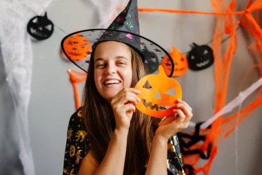 Cadılar Bayramı için parlak dekore edilmiş bir alanda neşeli bir cadı, balkabağı kesimi, renkli flamalar ve ürkütücü dekorlarla çevrili..