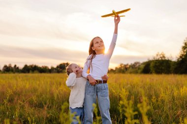 Gün batımında çayırda oynayan iki kız kardeş. Büyük kız oyuncak bir uçağı gökyüzüne doğru tutarken küçük olan ona hayranlık ve neşeyle bakıyor..
