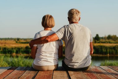 Güneş sakin nehrin üzerinde sessizce batarken bir çift, ahşap bir platformda oturuyor ve sakin bir atmosfer yaratıyor..