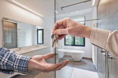  Emlakçı, boş fayanslı banyodaki alıcıya ev anahtarı veriyor.