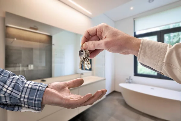 Realtor donnant la clé de maison à l'acheteur dans la salle de bain carrelée vide — Photo