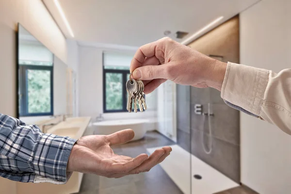 在空的瓷砖浴室把房子钥匙给买主的经纪人 免版税图库图片