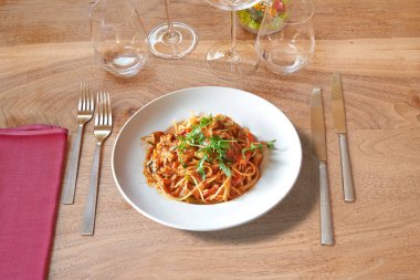 Kahverengi ahşap masaya gümüş çatal bıçak ve Linguine soslu beyaz tabak..