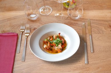 Kahverengi ahşap masada beyaz yuvarlak tabak ve sarımsaklı karides takımı..