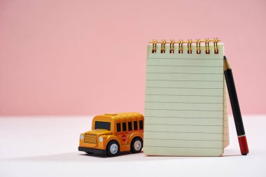 Oyuncak okul otobüsü ve pembe arka planda boş not defteri                              