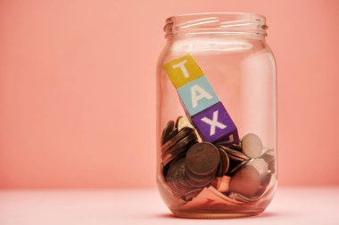 Pembe arka planda metin vergisi olan tasarruf kavanozu ve oyuncak bloğu.            