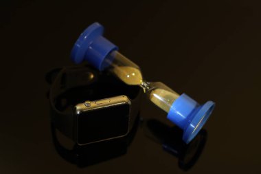 Elektronik saat ve kum saati siyah ayna masada yansıtılır