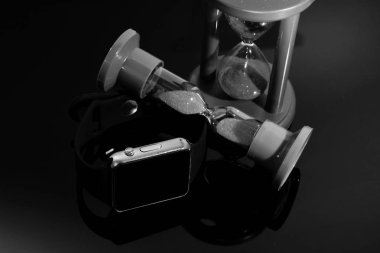 Elektronik saat ve kum saati siyah ayna masada yansıtılır