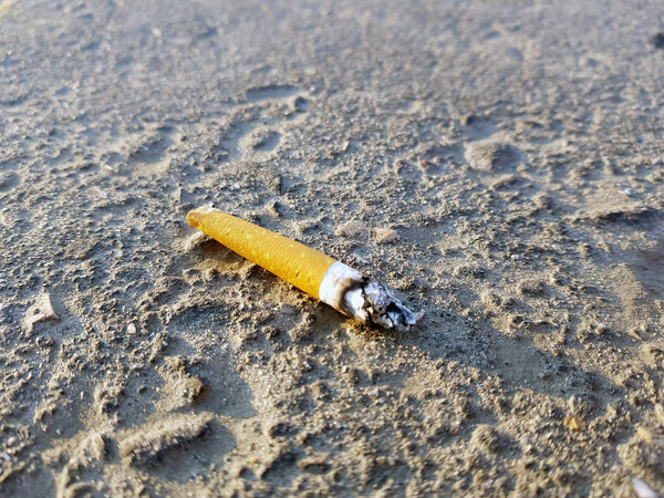 сигарета и окурок, лежащие на черном тротуаре зимой
