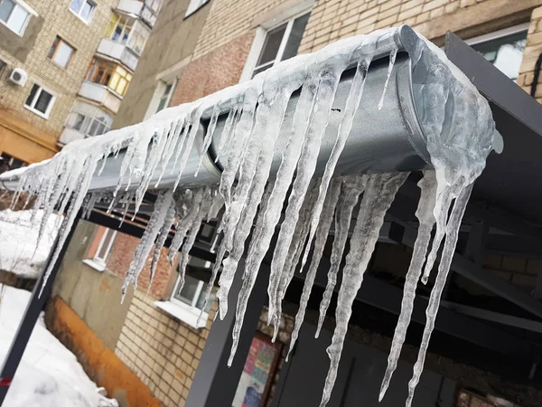 Große gefährliche Eiszapfen über dem Hauseingang im Winter oder Frühling gegen den Schnee — Stockfoto