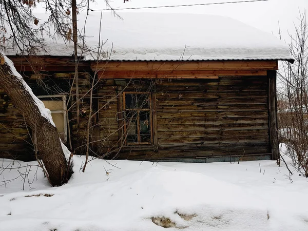 Старый заброшенный дом с разбитым окном на фоне снега зимой — стоковое фото