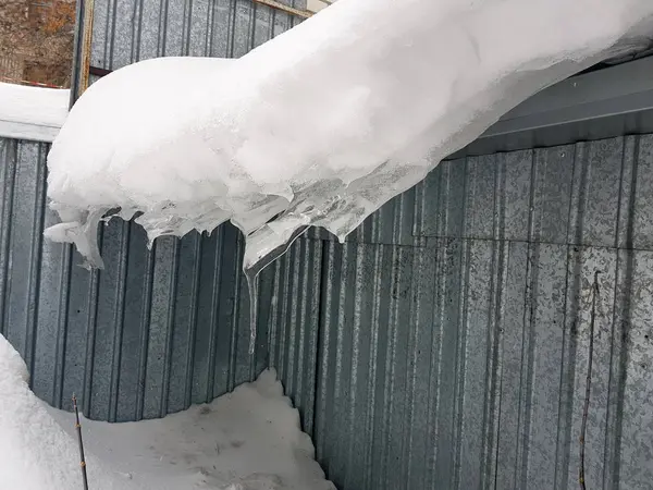 Nebezpečná ledová kostka s sněhu na střeše visí v zimě — Stock fotografie