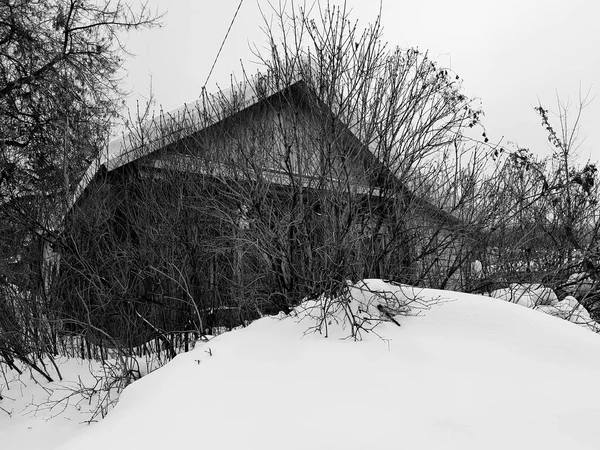 Velha casa abandonada com uma janela quebrada no fundo da neve no inverno — Fotografia de Stock