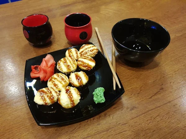 Hermosos rollos sabrosos en un plato negro con salsa de soja y palillos —  Fotos de Stock