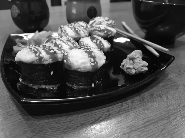 Beaux rouleaux savoureux sur une assiette noire avec sauce soja et baguettes — Photo