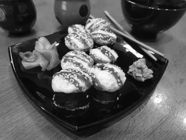 Beaux rouleaux savoureux sur une assiette noire avec sauce soja et baguettes — Photo