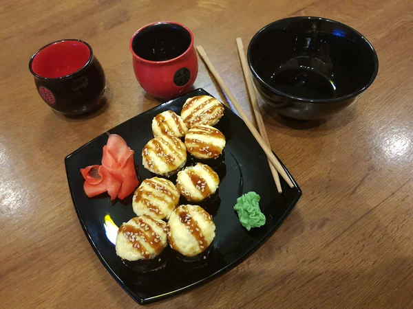 Beaux rouleaux savoureux sur une assiette noire avec sauce soja et baguettes — Photo