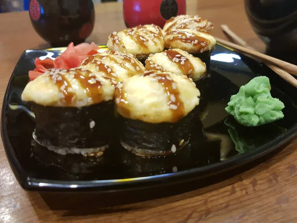 Beaux rouleaux savoureux sur une assiette noire avec sauce soja et baguettes — Photo