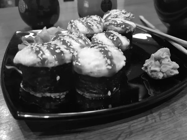 Hermosos rollos sabrosos en un plato negro con salsa de soja y palillos — Foto de Stock