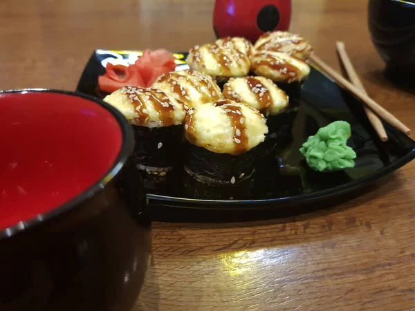 Hermosos rollos sabrosos en un plato negro con salsa de soja y palillos — Foto de Stock