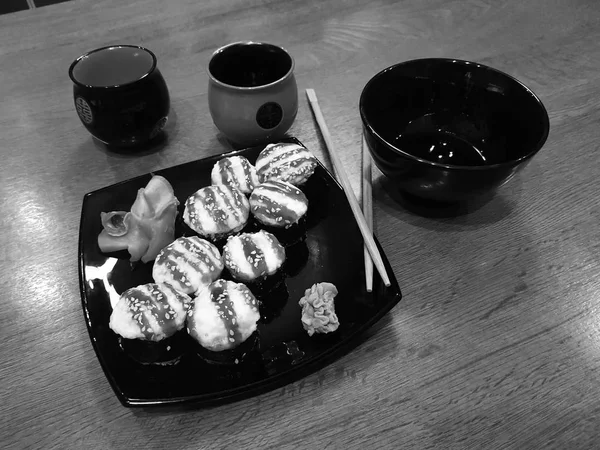 Beaux rouleaux savoureux sur une assiette noire avec sauce soja et baguettes — Photo