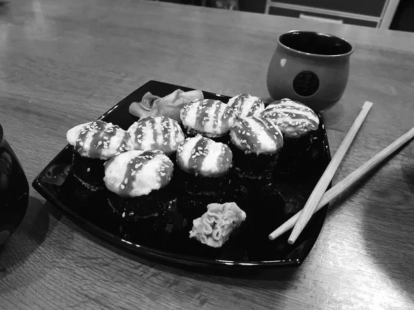 Beaux rouleaux savoureux sur une assiette noire avec sauce soja et baguettes — Photo