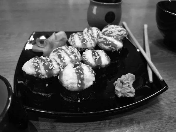 Hermosos rollos sabrosos en un plato negro con salsa de soja y palillos —  Fotos de Stock