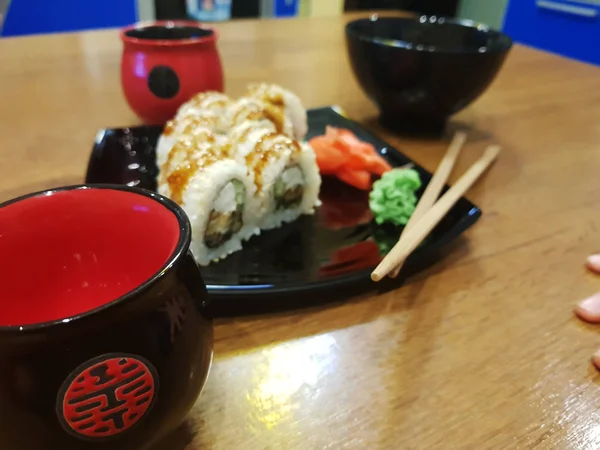 Beaux rouleaux savoureux sur une assiette noire avec sauce soja et baguettes — Photo