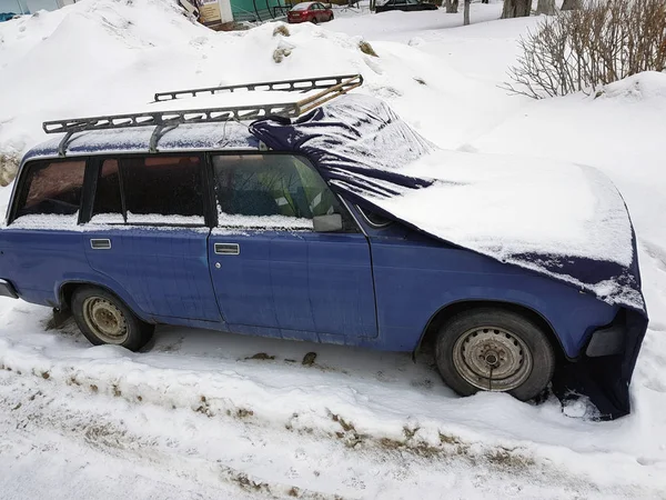 Старый автомобиль с крышкой на капоте в снегу — стоковое фото