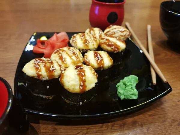 Beaux rouleaux savoureux sur une assiette noire avec sauce soja et baguettes — Photo