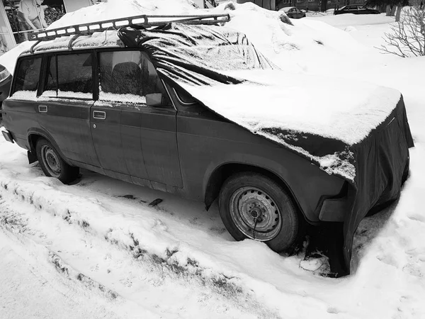 Старый автомобиль с крышкой на капоте в снегу — стоковое фото