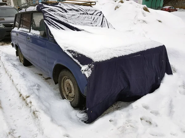 Старый автомобиль с крышкой на капоте в снегу — стоковое фото