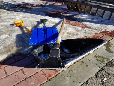 Bahar veya kış aylarında bir kiremit ve çit arka plana karşı karda kar kürek ve buz baltası