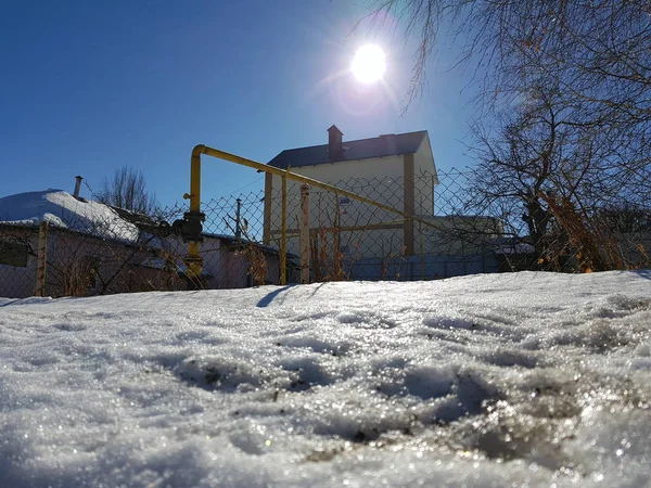 Snow csillog a napsugarak a háttérben a csővezeték és a házak a télen vagy tavasszal — Stock Fotó