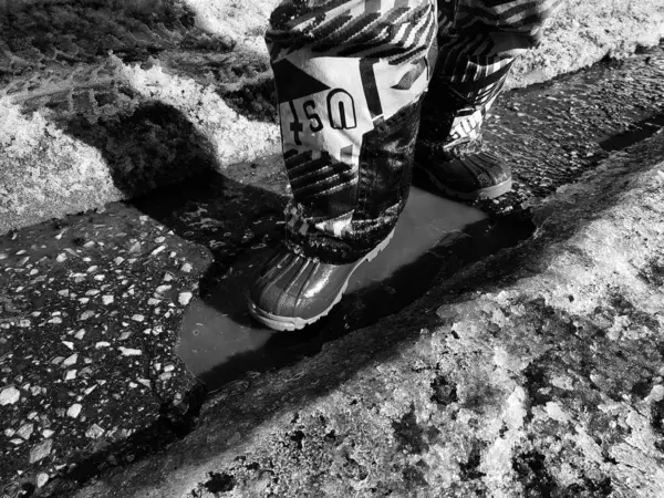 Uma criança caminha em botas através de poças na primavera ou inverno em tempo ensolarado . — Fotografia de Stock