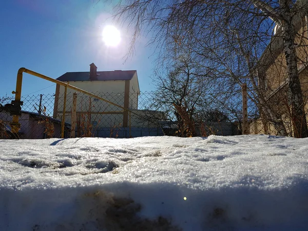 Сніг блищить в променях сонця на фоні трубопроводу і будинків взимку або навесні — стокове фото