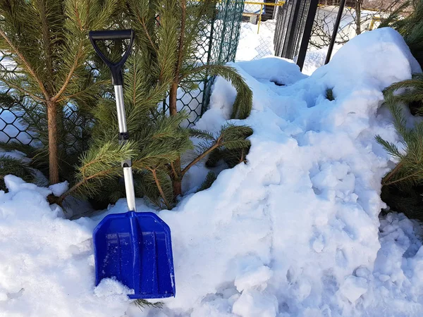 Una pala de nieve cuesta alrededor de una montaña de nieve y un árbol de Navidad en invierno o primavera Imagen de archivo