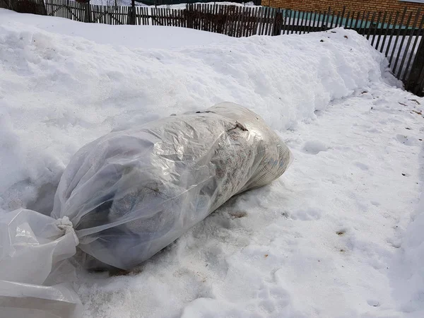 A large package of garbage lies right on the road against the backdrop of snow in winter