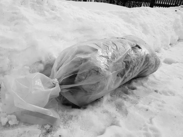 A large package of garbage lies right on the road against the backdrop of snow in winter