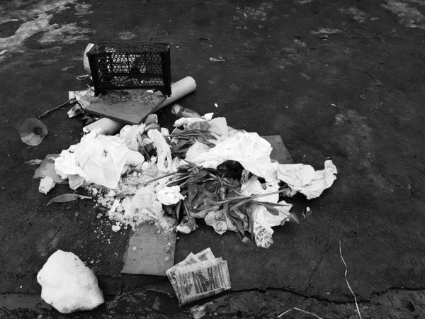 Garbage - scattered flowers, packages, boxes on the snow and on the asphalt in winter or spring