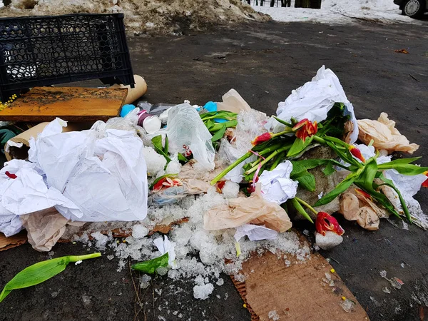 Garbage - scattered flowers, packages, boxes on the snow and on the asphalt in winter or spring