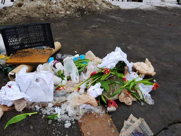 Garbage - scattered flowers, packages, boxes on the snow and on the asphalt in winter or spring